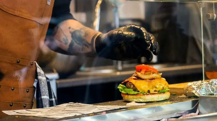 Hand mit schwarzem Handschuh plattiert einen Cheeseburger